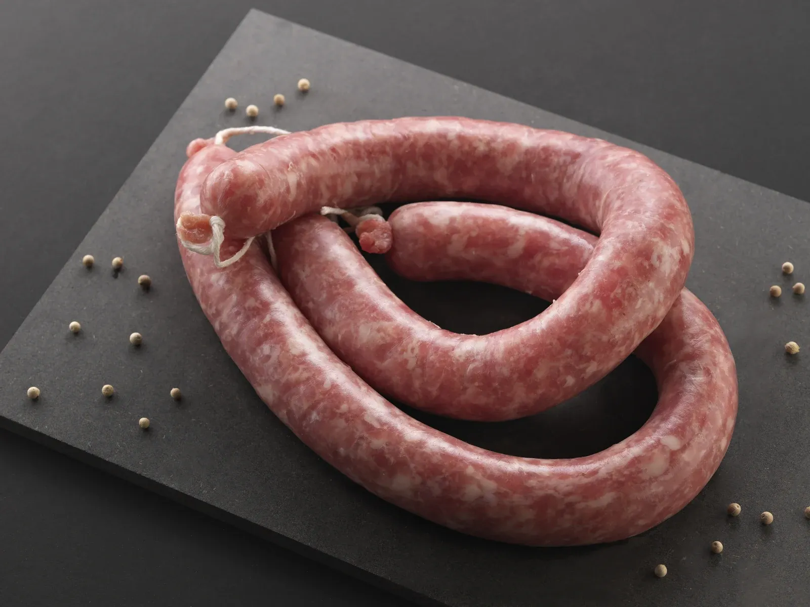 Botifarra crua enrotllada, lligada amb cordill, amb grans de pebre escampats al voltant